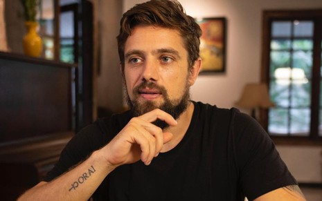 Rafael Cardoso com camiseta preta, olha para a esquerda em foto em sua casa
