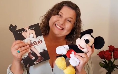 Carina Rissi segura o livro Perdida em uma mão e um boneco do Mickey em outra
