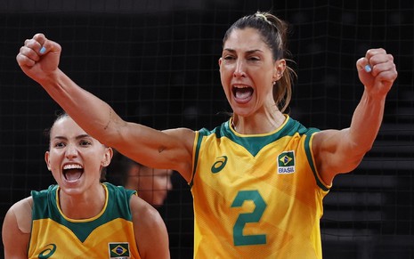 Carol Gattaz vibra em jogo do Brasil contra a Rússia, ela usa uma camisa verde e amarela, com Gabi atrás comemorando um ponto da central