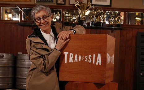 Cassia Kis está encostada em uma caixa de madeira com o nome da novela Travessia
