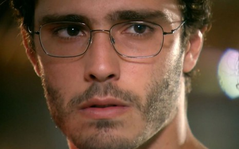 O ator Thiago Rodrigues como Cassiano em A Favorita; ele está de óculos olhando de atravessado com ar de mistério