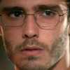 O ator Thiago Rodrigues como Cassiano em A Favorita; ele está de óculos olhando de atravessado com ar de mistério
