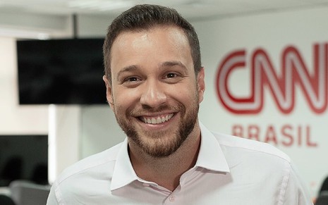 Cassius Zeilmann com um sorriso e uma blusa rosa na Redação da CNN Brasil em SP