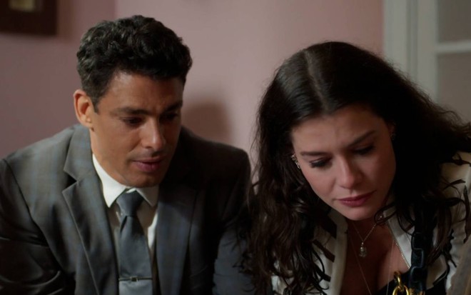 Cauã Reymond e Alinne Moraes surgem lado a lado e olham para baixo em cena de Um Lugar ao Sol