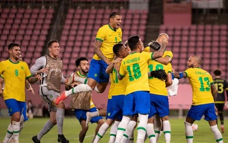 Foto do time de futebol masculino do Brasil se abraçando reunido em campo durante partida