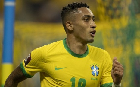 Jogador Raphinha, da seleção brasileira, vestindo uniforme verde e amarelo, e comemorando gol feito em partida
