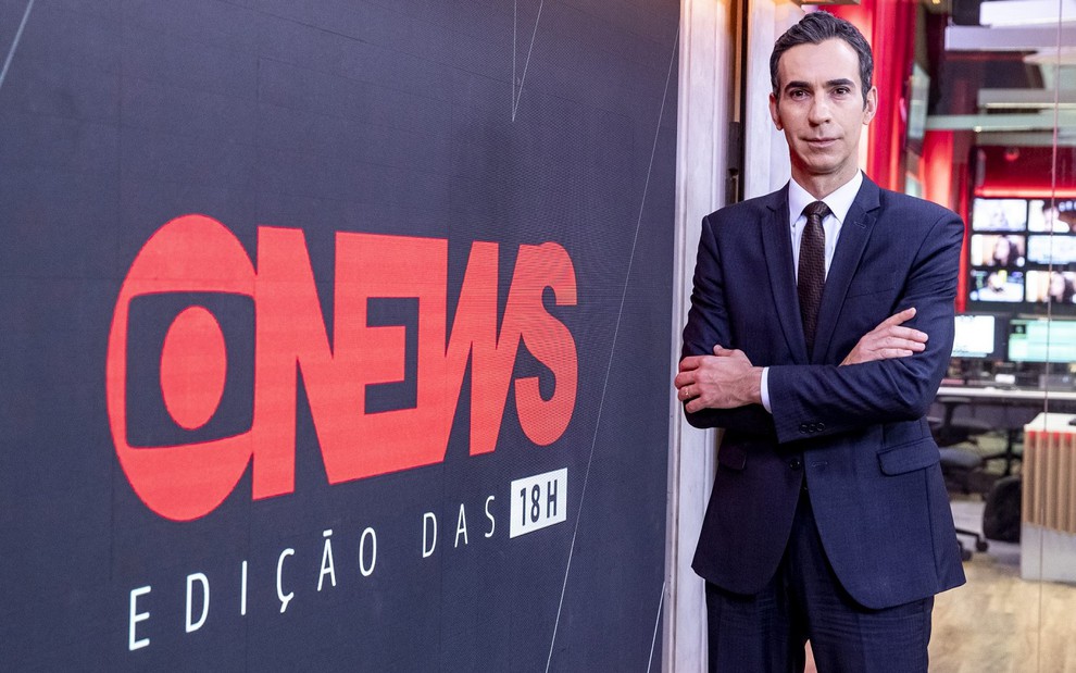 César Tralli usa um terno azul, uma gravata marrom e uma camisa branca cruza os braços nos estúdios da GloboNews
