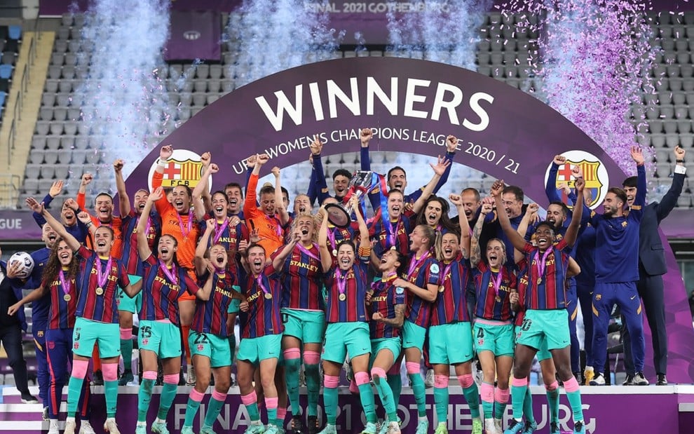 Jogadoras do Barcelona, com uniforme grená do clube e levantando as mãos para cima de alegria, erguendo o troféu da Uefa Women's Champions League da temporada 2020/2021