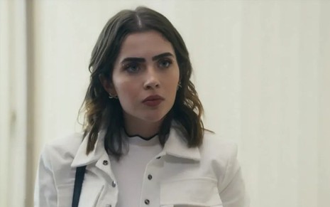 Em cena de Travessia, Jade Picon está com expressão de susto; ela veste jaqueta e blusa branca