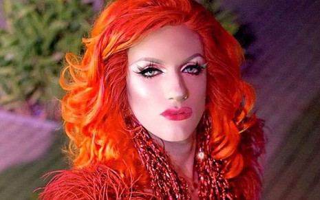 Com uma peruca vermelha e roupa da mesma cor, a drag queen Chloe V. faz bico