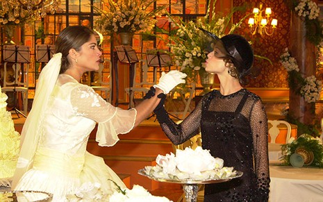 As atrizes Priscila Fantin e Mariana Ximenes como Olga e Ana Francisca em Chocolate com Pimenta; elas estão frente a frente enquanto a primeira, vestida de noiva, olha com cara de séria para ela e estende a mão, que é segurada pela segunda