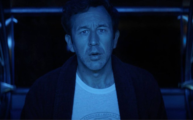 Chris O'Dowd com cara de assustado e fundo azul