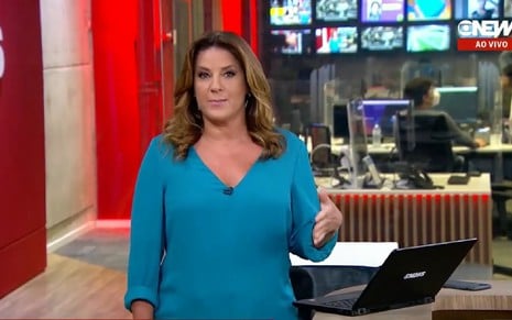 Christiane Pelajo com uma blusa azul, nos estúdios da Globo em São Paulo, olhando para a esquerda e ao horizonte, observando algo fora do plano da câmera: jornalista é apresentadora da GloboNews