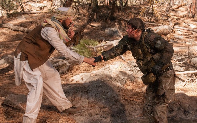 Um cidadão afegão estende a mão para Mark Wahlberg, que está machucado, e o ajuda, enquanto faz sinal de silêncio com um dedo na boca