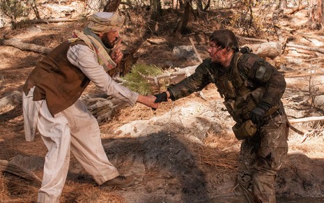 Um cidadão afegão estende a mão para Mark Wahlberg, que está machucado, e o ajuda, enquanto faz sinal de silêncio com um dedo na boca