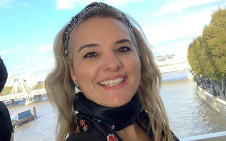 Debora Ribeiro em foto publicada no Instagram, sorrindo, em frente a paisagem externa