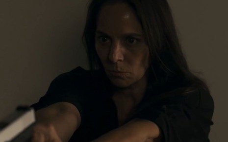Claudia Mauro com expressão séria e apontando arma em cena como Pilar na novela Travessia