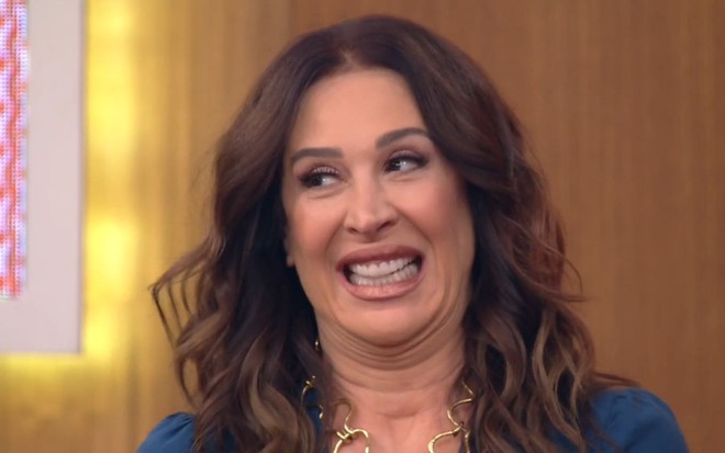 Claudia Raia no estúdio do Encontro com Fátima Bernardes; ela veste uma blusa azul e está com um sorriso constrangido