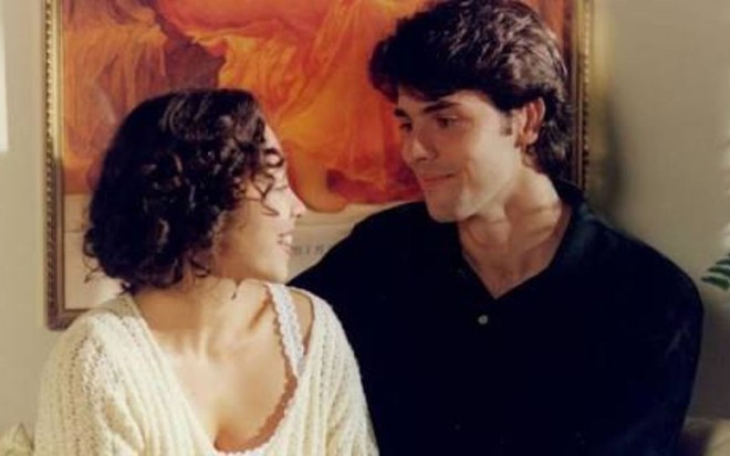 A atriz Carla Marins e o ator Claudio Lins lado a lado, se olhando e com leves sorrisos em cena da novela História de Amor (1995)