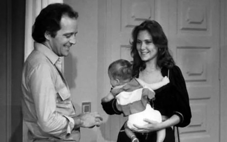 Cláudio Marzo e Elizabeth Savala, que segura um bebê no colo, em foto preto e branco da novela Plumas e Paetês