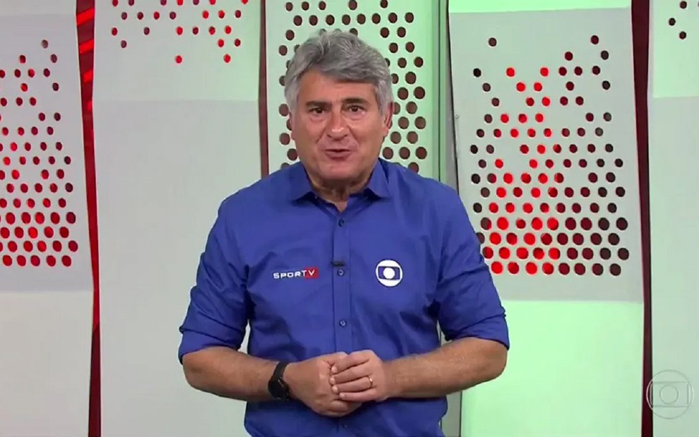 Cleber Machado com uma blusa azul em uma transmissão de futebol na Globo