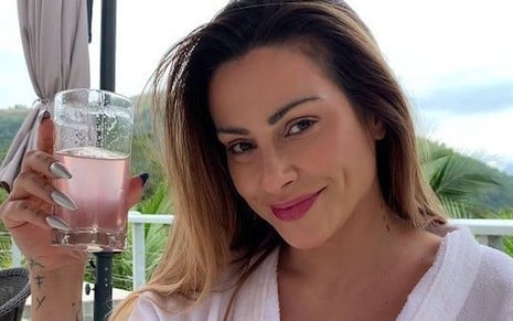 A atriz Cleo segura um copo com líquido cor de rosa e posa sorrindo em foto postada em rede social