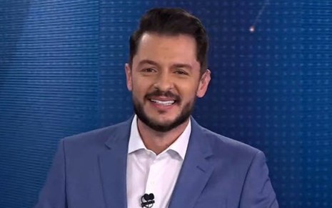 O repórter da CNN Brasil Renan Fiuza está de terno na bancada de um programa