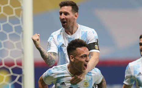 Montado nas costas de Lautaro Martínez, Lionel Messi cerra o punho ao comemorar gol da Argentina