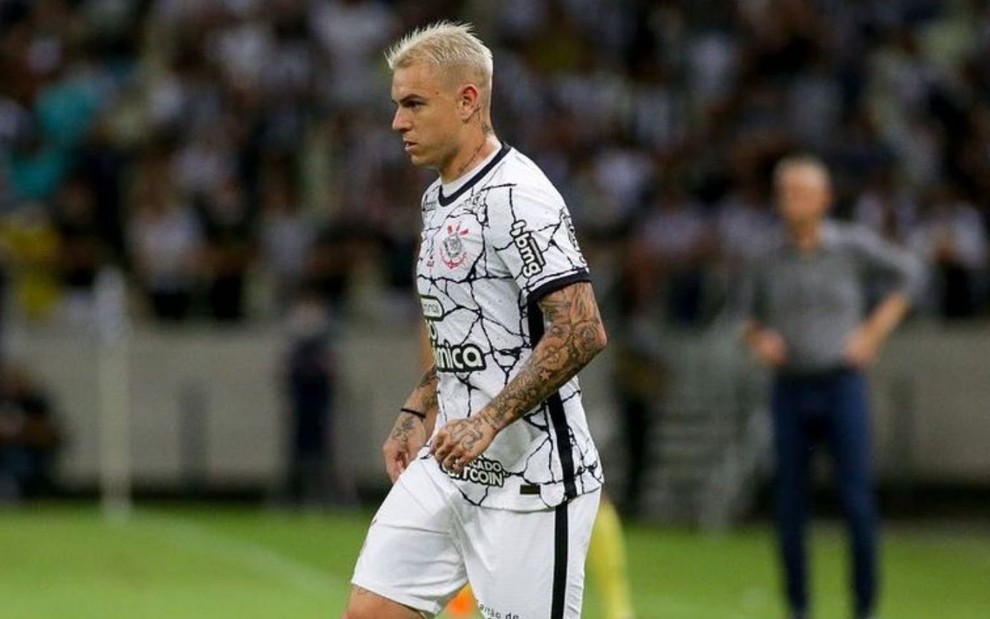 Jogador Róger Guedes, do Corinthians, vestindo uniforme branco com detalhes preto, com a bola aos pés