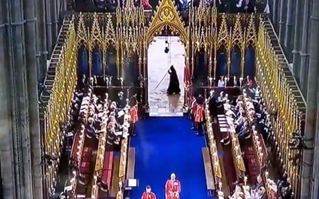 Um figura de preto com um cajado passa ao fundo da abadia de Westminster na coroação de Charles 3º