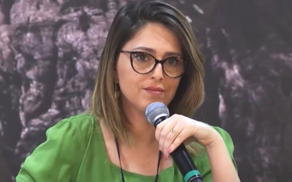 Com uma blusa verde e óculos, Cristiane Cardoso fala ao microfone