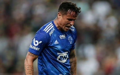 Jogador Edu, do Cruzeiro, grita em campo e veste uniforme azul com detalhes brancos