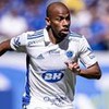 Jogador Waguininho, do Cruzeiro, corre em campo e veste uniforme branco com detalhes azuis