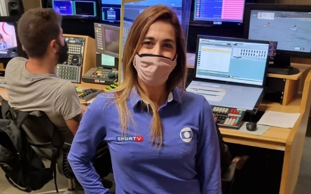 Daniele Hypolito usa o uniforme azul com o logo da Globo e do SporTV; ela usa máscara no rosto e aparece na frente de telas de computadores