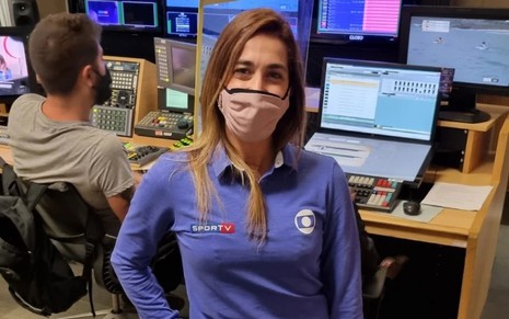 Daniele Hypolito usa o uniforme azul com o logo da Globo e do SporTV; ela usa máscara no rosto e aparece na frente de telas de computadores