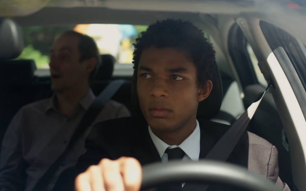 Ator Juan Paiva surge ao volante de carro, com o ator Daniel Dantas no banco de trás, em cena de Um Lugar ao Sol