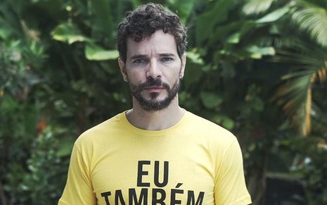 Daniel de Oliveira posa comm blusa amarela e expressão séria