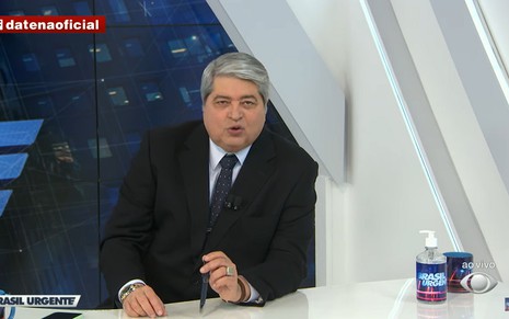 O apresentador José Luiz Datena com um terno preto e uma gravata azul, falando com o público do Brasil Urgente