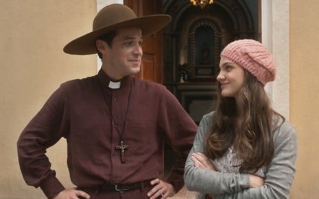 Os atores Jayme Matarazzo e Débora Ozório estão caracterizados como seus personagens em Além da Ilusão e se olhando; ele está vestido como padre e chapéu e ela usa boina