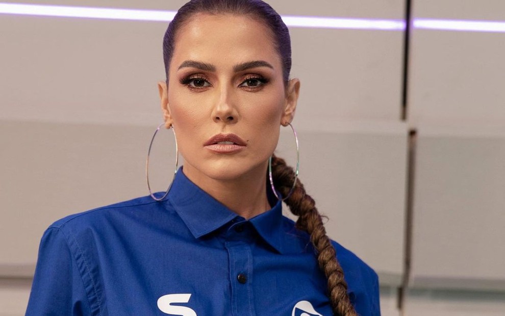 Deborah Secco com expressão séria, brincos de argola e camisa azul, posa para foto em estúdio do SporTV