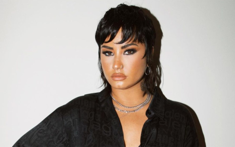Demi Lovato com blusa preta decotada em frente a fundo claro