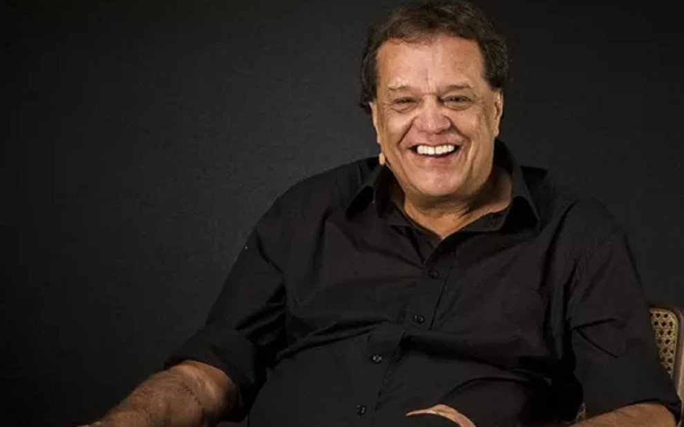 Dennis Carvalho com uma camisa preta e um sorriso em uma coletiva na Globo