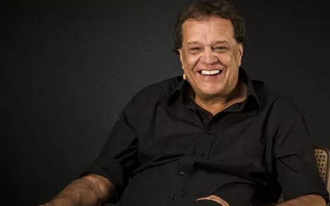 Dennis Carvalho com uma camisa preta e um sorriso em uma coletiva na Globo