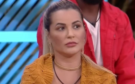 Foto mostra Deolane olhando para o lado; ela veste blusa laranja