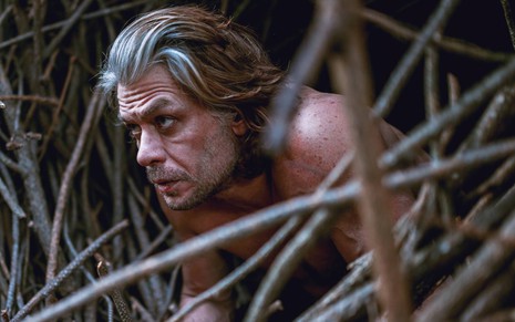 Fabio Assunção de cabelos grisalhos, sem camisa, em meio a matagal em cena da série Desalma