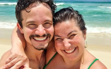 Diego Braga e Mariana Xavier estão numa praia e sorriem para a câmera