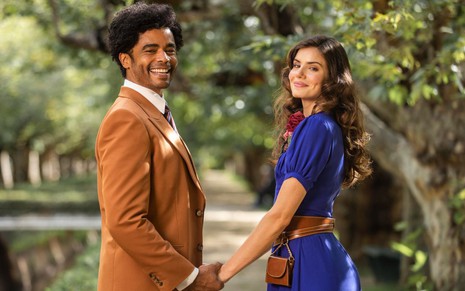 Diogo Almeida e Camila Queiroz estão de mãos dadas e posam para foto caracterizados com roupas de época