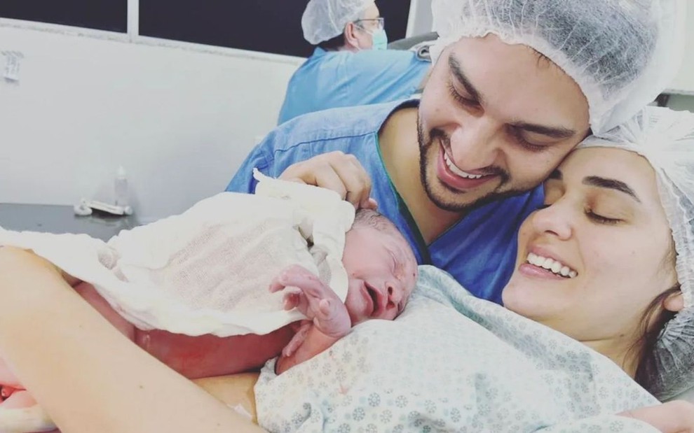 Diogo Mussi, bebê Luca e Bruna em maternidade; adultos vestem roupa e touca cirúrgica