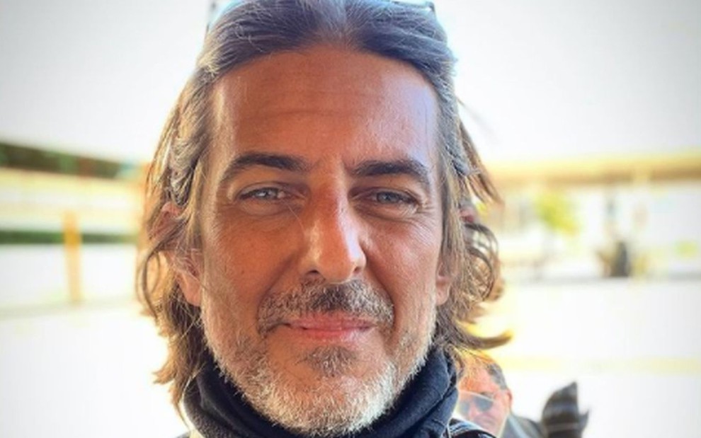 Adriano Melo de cabelo comprido, preso para trás pelos óculos e barba grisalha