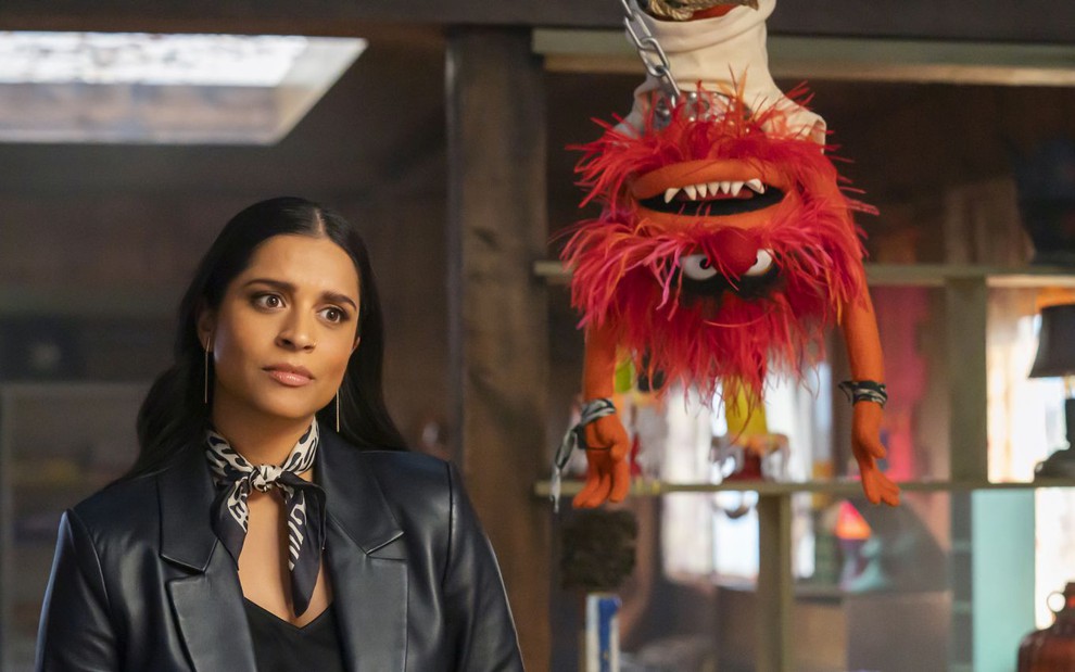 Lilly Singh tem expressão séria em cena de Muppets e o Caos Elétrico ao lado do Animal, que está de cabeça para baixo